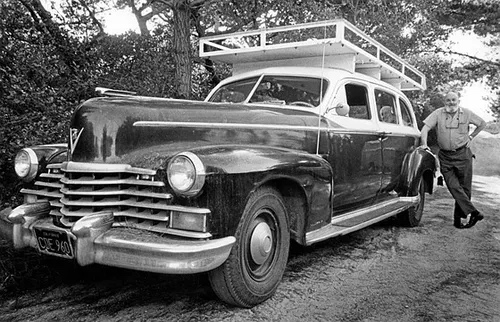 Adams leaning against dark Cadillac with white wooden roof platform