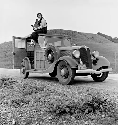 Young woman sitting on roof of 1930s Ford vehicle with sketchbook