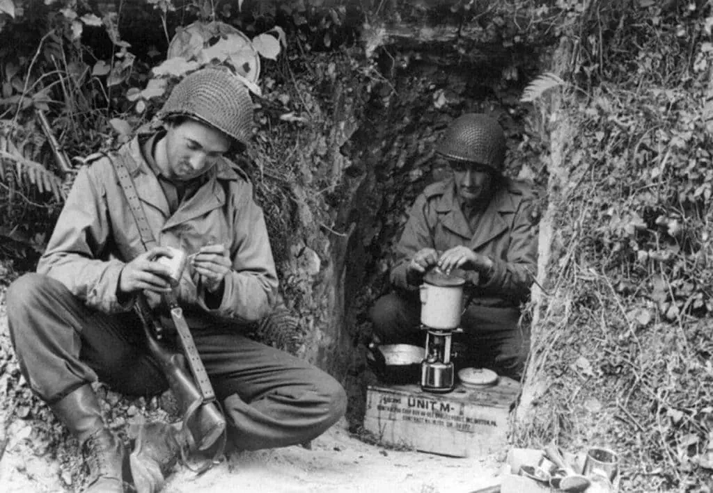 Two soldiers in a foxhole using a Coleman camp stove, WWII Europe